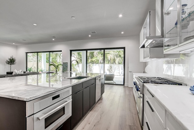 kitchen with appliances with stainless steel finishes, sink, light stone countertops, white cabinetry, and light hardwood / wood-style flooring