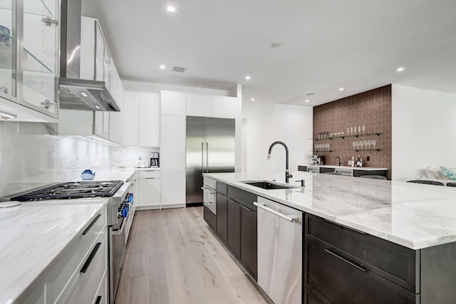 kitchen with sink, light hardwood / wood-style floors, white cabinets, high end appliances, and a center island with sink