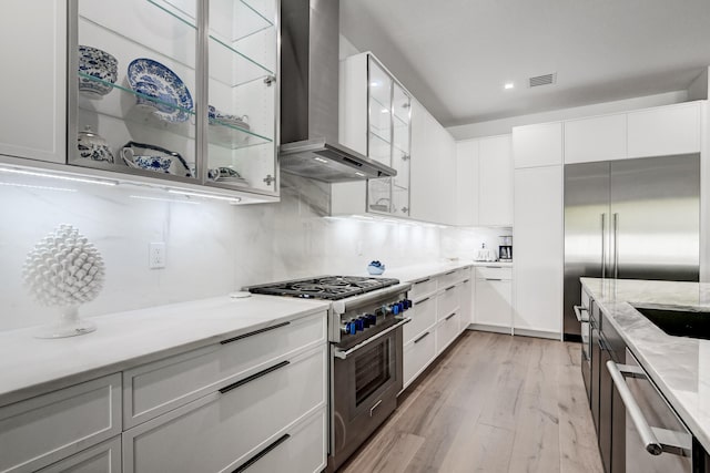 kitchen featuring appliances with stainless steel finishes, wall chimney range hood, light hardwood / wood-style flooring, and white cabinetry