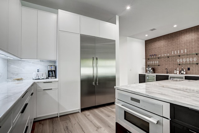 kitchen with decorative backsplash, white cabinets, appliances with stainless steel finishes, light stone counters, and light hardwood / wood-style floors