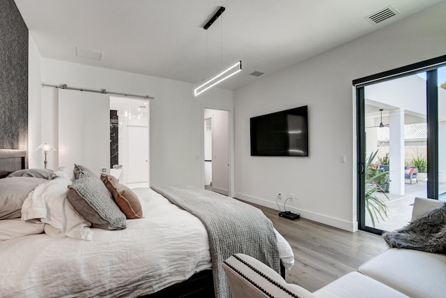 bedroom featuring access to outside, a barn door, and light wood-type flooring