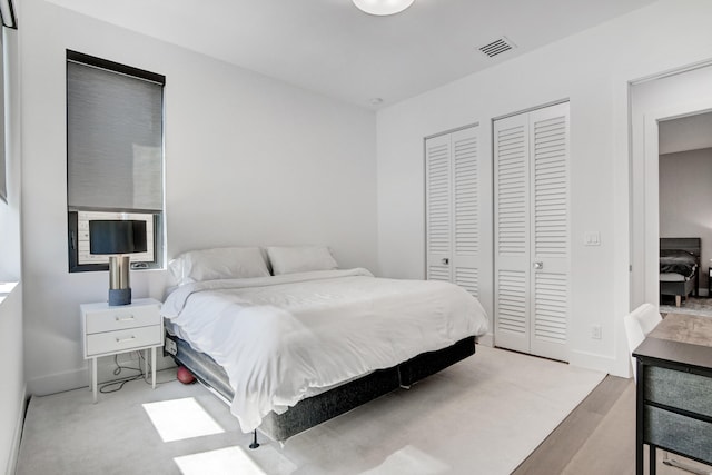 bedroom with light hardwood / wood-style flooring and two closets