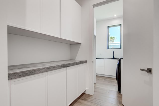 bar featuring washer / dryer, white cabinets, and light hardwood / wood-style floors