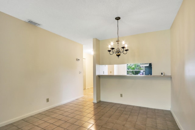 spare room with tile patterned flooring, a textured ceiling, and a notable chandelier