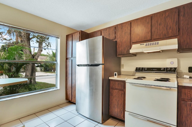 kitchen featuring light tile patterned flooring, stainless steel refrigerator, a healthy amount of sunlight, and white electric stove