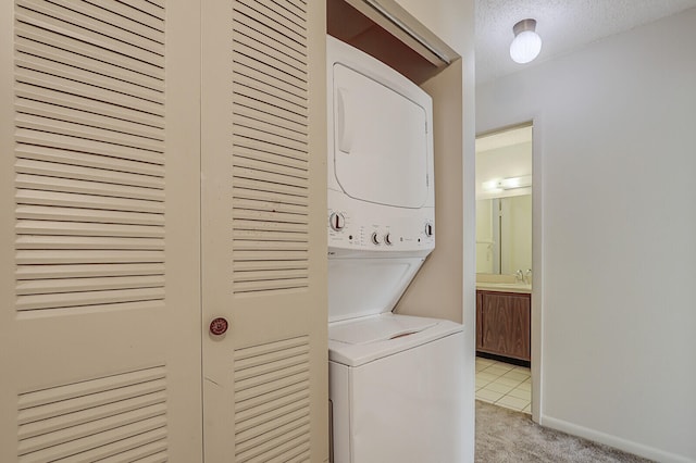 laundry area featuring sink, stacked washing maching and dryer, a textured ceiling, and light colored carpet