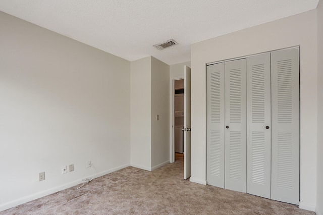 unfurnished bedroom featuring a textured ceiling, light carpet, and a closet