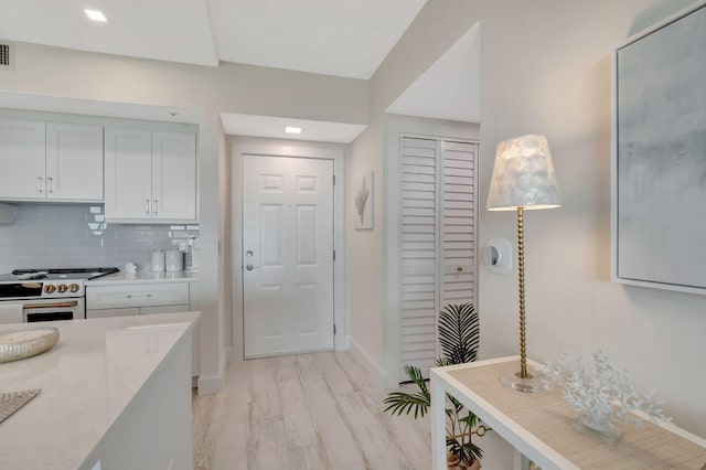 kitchen with light hardwood / wood-style flooring, white range with gas cooktop, white cabinetry, light stone countertops, and tasteful backsplash