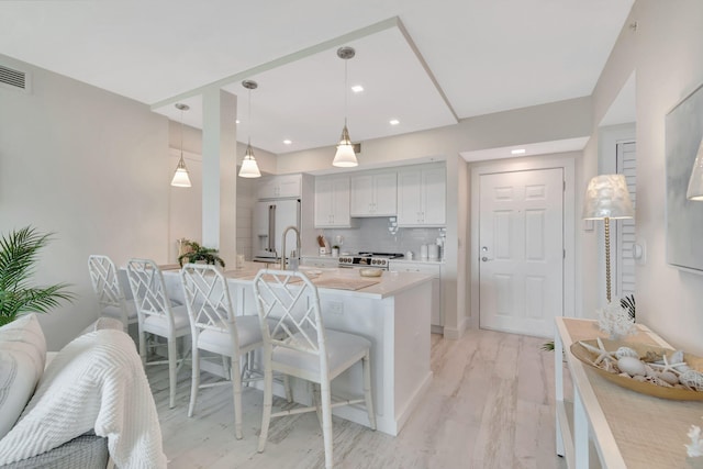 kitchen with white cabinets, hanging light fixtures, high end refrigerator, a breakfast bar area, and decorative backsplash