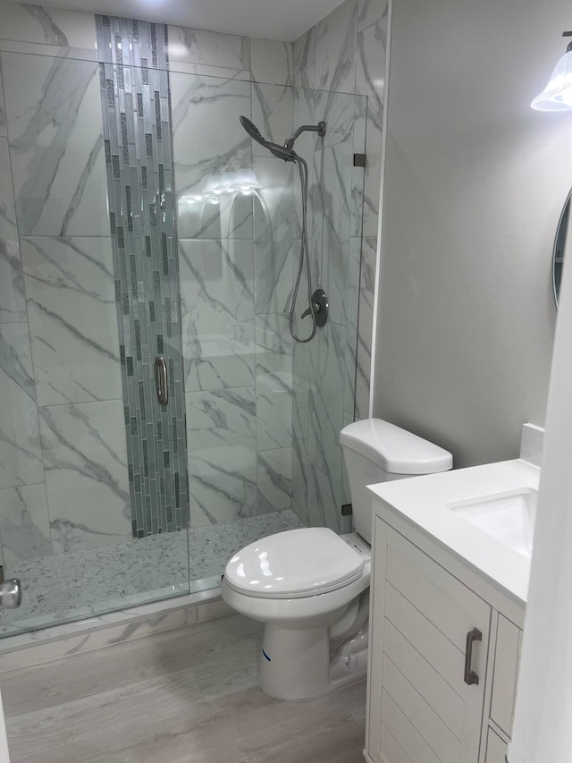 bathroom featuring vanity, a shower with shower door, hardwood / wood-style floors, and toilet