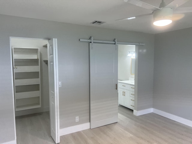 14910 Wildflower Ln, Delray Beach, FL 33446 - unfurnished bedroom with light wood finished floors, a barn door, a walk in closet, baseboards, and ceiling fan