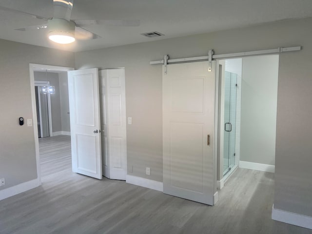 unfurnished bedroom featuring a barn door, light wood-type flooring, and ceiling fan