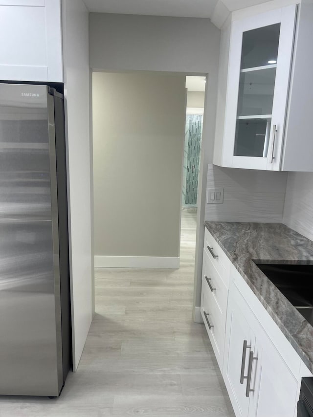 kitchen with light hardwood / wood-style flooring, stainless steel refrigerator, dark stone counters, and white cabinets