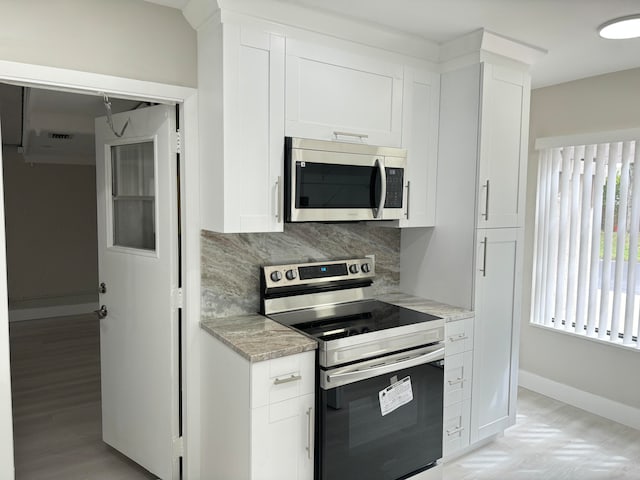 kitchen with appliances with stainless steel finishes, white cabinetry, light stone countertops, and backsplash