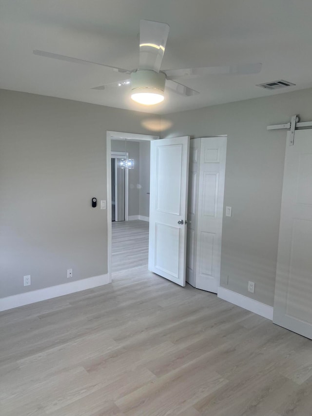 unfurnished room featuring light hardwood / wood-style floors, a barn door, and ceiling fan