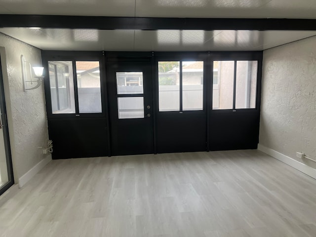 empty room with light wood-type flooring, beamed ceiling, and plenty of natural light