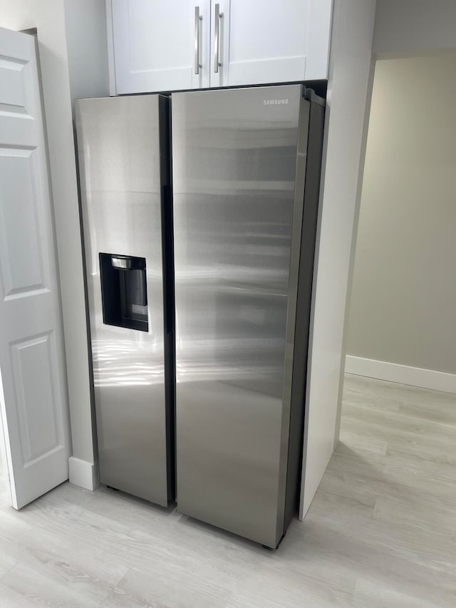 interior details featuring white cabinetry, stainless steel fridge, and light hardwood / wood-style floors