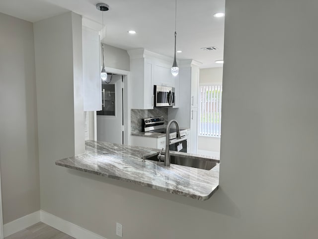 kitchen featuring light stone counters, appliances with stainless steel finishes, white cabinetry, sink, and decorative light fixtures