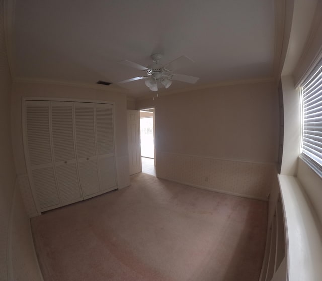 unfurnished bedroom with crown molding, ceiling fan, a closet, and light colored carpet