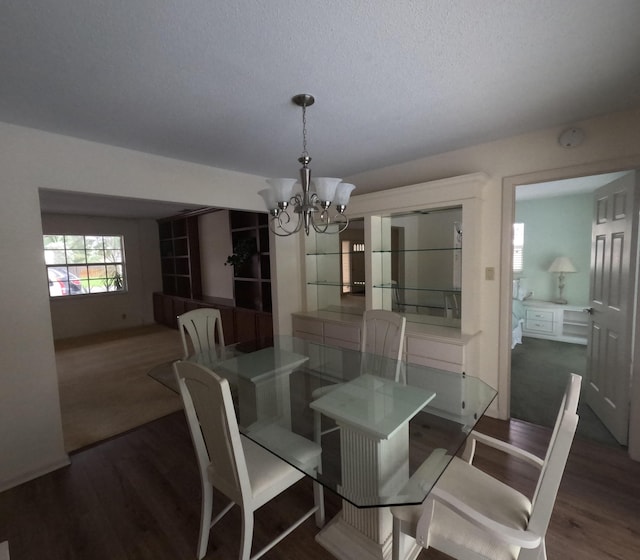 dining area with dark wood-type flooring, a textured ceiling, and a notable chandelier