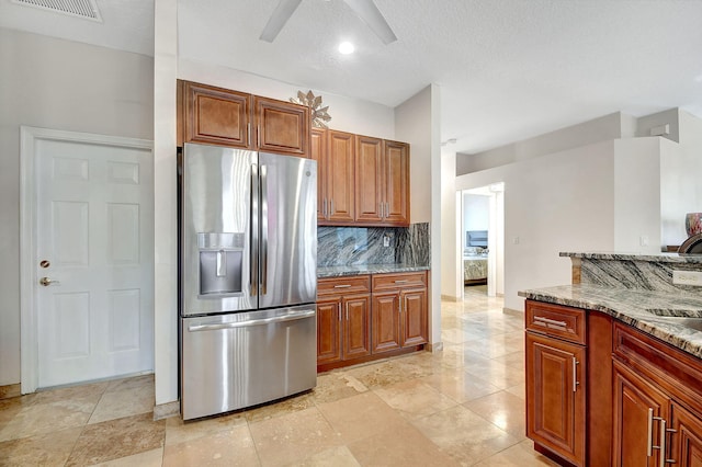 kitchen featuring decorative backsplash, stainless steel fridge, light stone countertops, and a textured ceiling