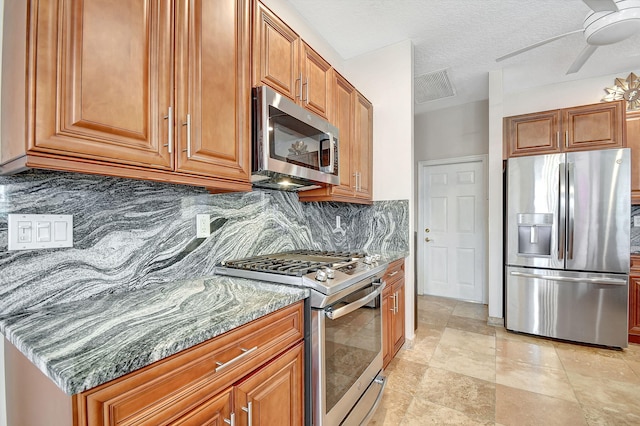 kitchen featuring tasteful backsplash, a textured ceiling, ceiling fan, stainless steel appliances, and dark stone counters