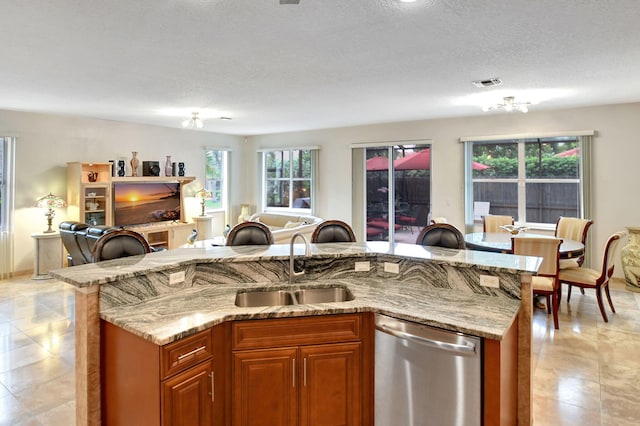 kitchen featuring stainless steel dishwasher, sink, a kitchen island with sink, and a textured ceiling