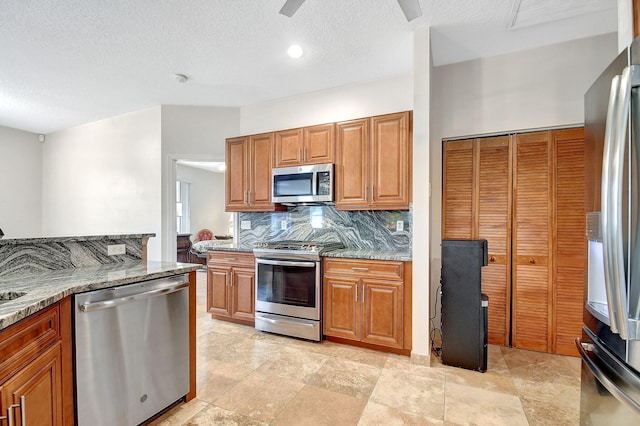 kitchen featuring a textured ceiling, light stone counters, stainless steel appliances, and backsplash