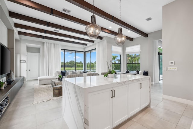 kitchen with a wealth of natural light, beamed ceiling, a kitchen island, and white cabinetry