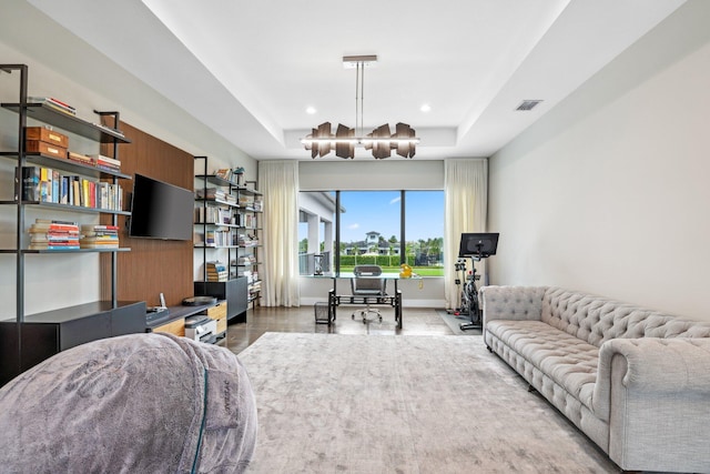 living room with an inviting chandelier, wood-type flooring, and a raised ceiling