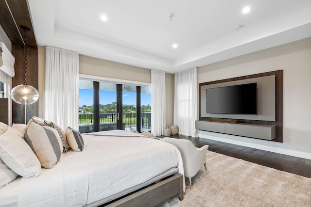 bedroom with dark wood-type flooring, a tray ceiling, and access to outside