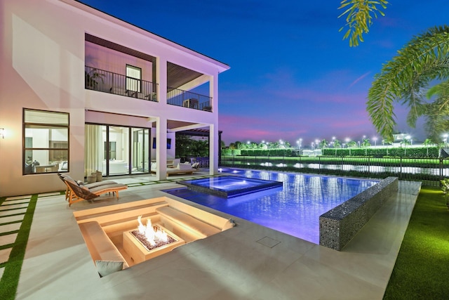 pool at dusk with a patio, a fire pit, and a water view