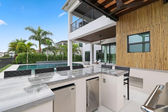 view of patio with ceiling fan, a balcony, and a swimming pool with hot tub