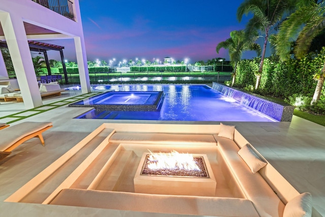 pool at dusk with an in ground hot tub, a water view, pool water feature, a fire pit, and a patio