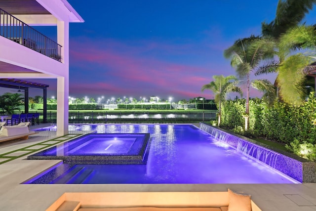 pool at dusk featuring a water view, an in ground hot tub, pool water feature, and a patio area