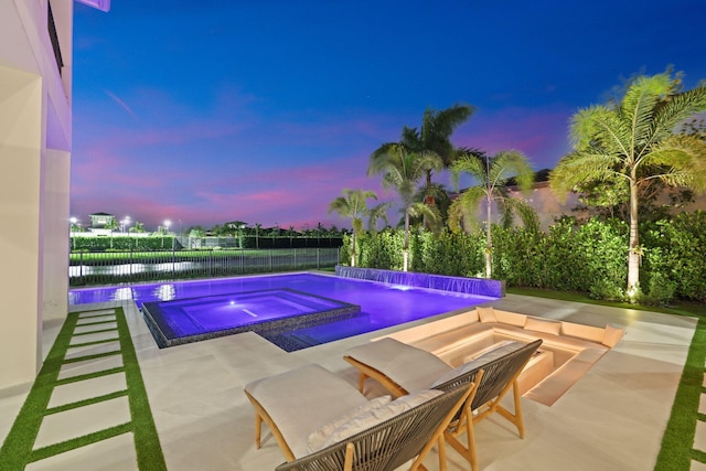 pool at dusk with a water view, an in ground hot tub, pool water feature, and a patio