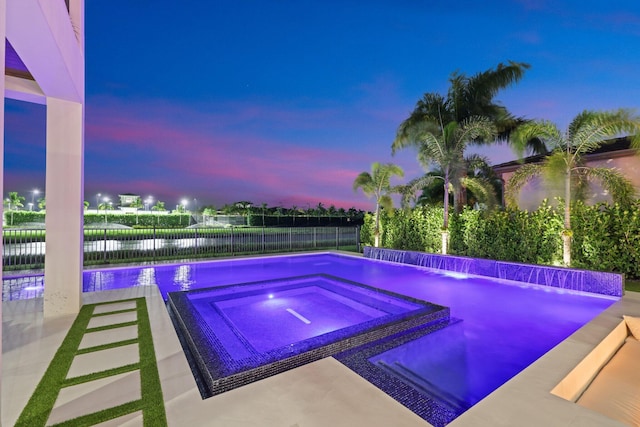 pool at dusk with a patio, an in ground hot tub, pool water feature, and a water view