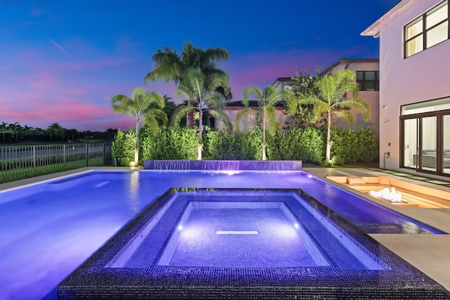 pool at dusk featuring an in ground hot tub and pool water feature