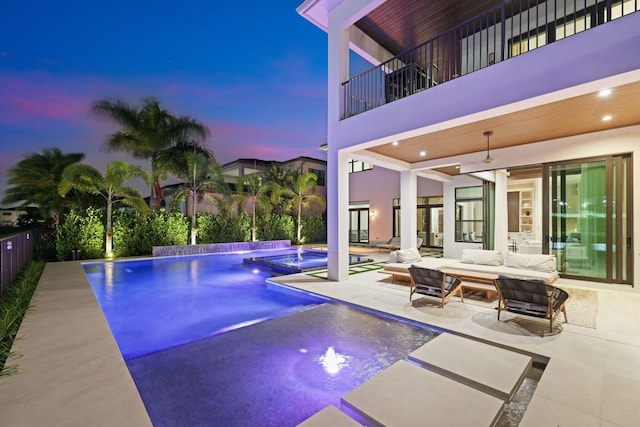 pool at dusk with a patio area, pool water feature, outdoor lounge area, and ceiling fan