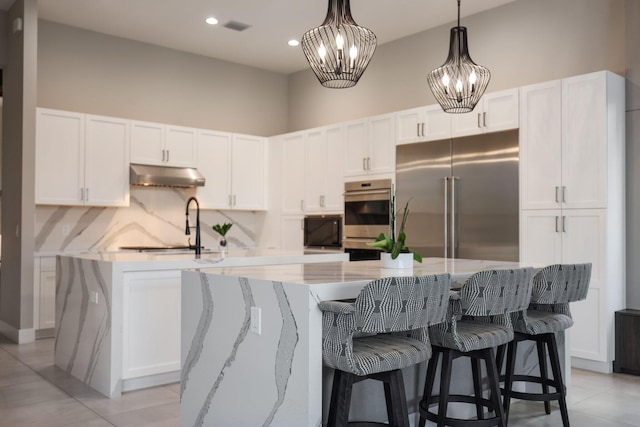 kitchen featuring a large island with sink, appliances with stainless steel finishes, pendant lighting, and white cabinetry