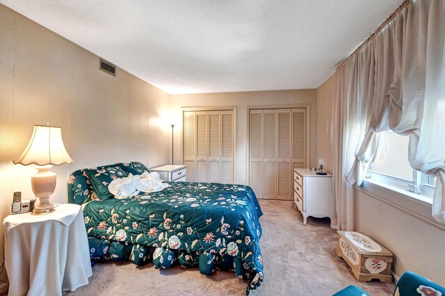 bedroom featuring a textured ceiling, two closets, and light colored carpet