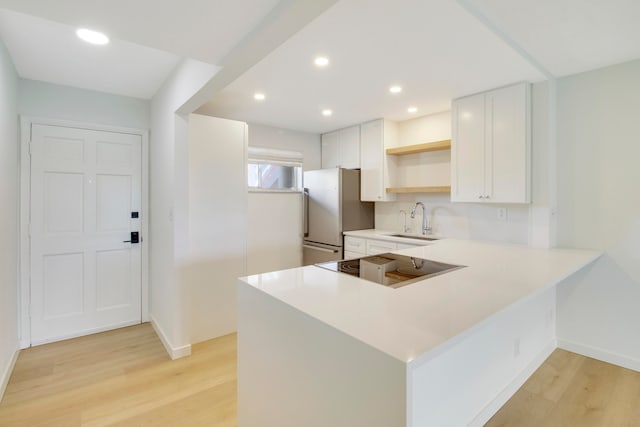 kitchen featuring kitchen peninsula, stainless steel fridge, white cabinetry, light hardwood / wood-style floors, and sink