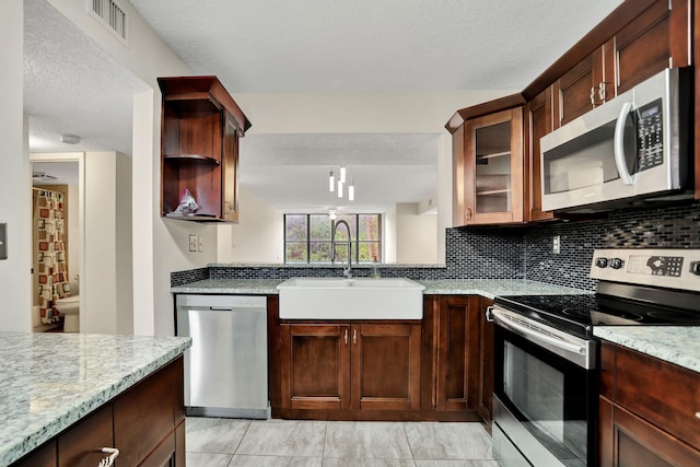 kitchen featuring a textured ceiling, sink, light stone counters, and appliances with stainless steel finishes