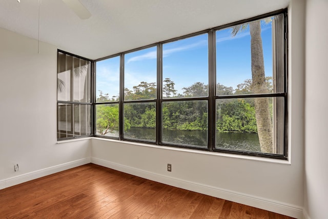 spare room featuring hardwood / wood-style flooring, ceiling fan, a healthy amount of sunlight, and a water view