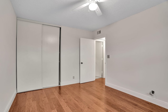 unfurnished bedroom with a closet, light hardwood / wood-style floors, a textured ceiling, and ceiling fan