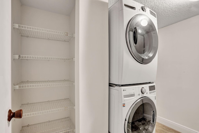 laundry area with stacked washer and clothes dryer, a textured ceiling, and light wood-type flooring