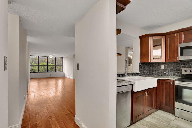 kitchen with stainless steel appliances, a textured ceiling, tasteful backsplash, sink, and light wood-type flooring