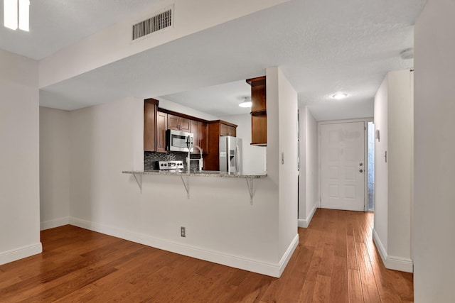 kitchen featuring tasteful backsplash, light wood-type flooring, appliances with stainless steel finishes, a textured ceiling, and kitchen peninsula