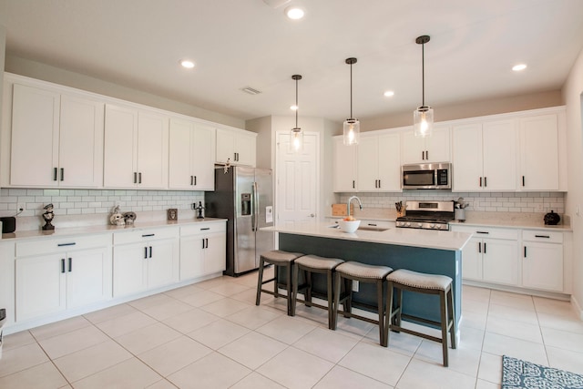 kitchen with appliances with stainless steel finishes, white cabinetry, decorative light fixtures, a breakfast bar, and a kitchen island with sink