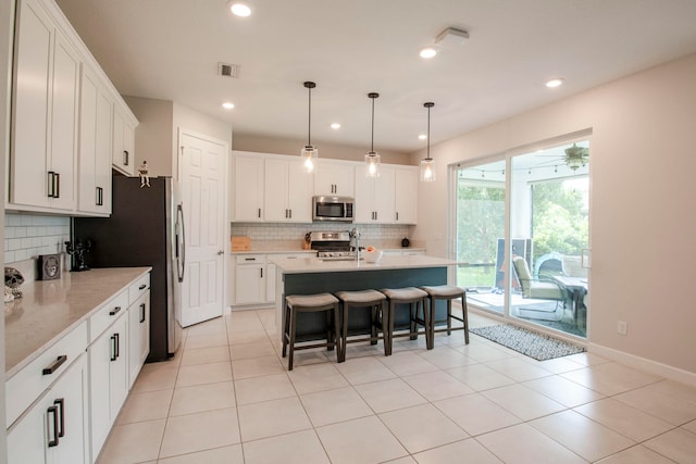 kitchen with white cabinets, backsplash, appliances with stainless steel finishes, a kitchen island with sink, and pendant lighting